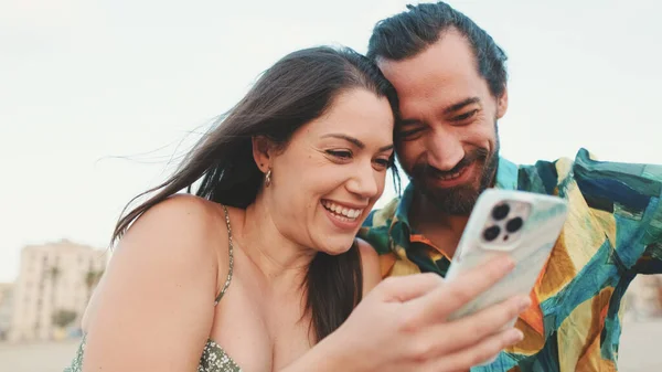 Casal Jovem Usa Telefone Celular Enquanto Sentado Praia Prédios Fundo — Fotografia de Stock