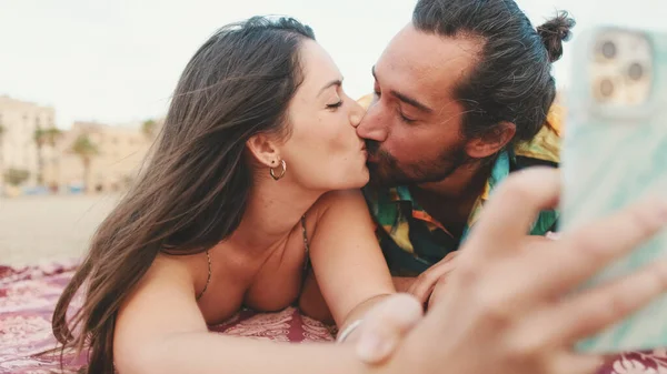 Man and woman kissing and making video call using mobile phone on the beach