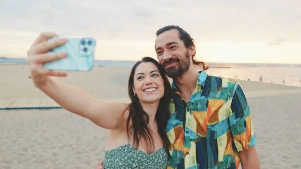在海滩上一边站着一边笑一边用手机自拍的夫妻 — 图库照片