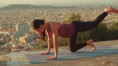 Young woman on her knee on mat with raised arm and leg on the observation deck