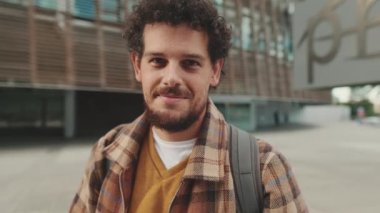 Close up, guy student stands outside the university building looks at the camera and smiles