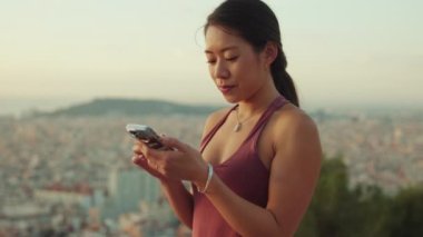 Şafak vakti gözetleme noktasında dururken cep telefonu kullanan mutlu atletik kadın.