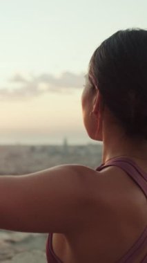 Yakından bakınca, vücut kıyafetli genç bir kadın güneş doğarken yoga pratiği yapıyor. Kız nilüfer pozisyonunda otururken ellerini kaldırır. Arka plan