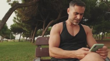 Spor giyim sektöründe gülen orta yaşlı adam cep telefonundan mesajlar okuyor.