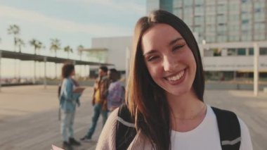 Student with notebooks in her hands looks at the camera and smiles