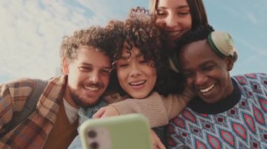 Mutlu gülümseyen arkadaşlar komik cep telefonu videoları izliyorlar.
