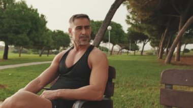 Olgun bir erkek parkta otururken spor kıyafetleri giymekten zevk alır.