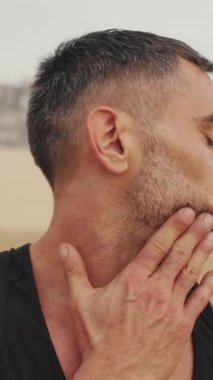 Adam plajda spor yapıyor ve boyun kaslarını esnetiyor.