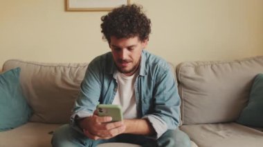 Üzgün adam koltukta oturuyor ve cep telefonu kullanıyor.