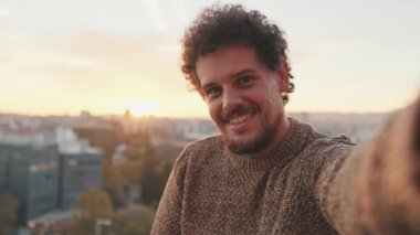 Mutlu genç adam balkonda durur, cep telefonundan selfie çeker.