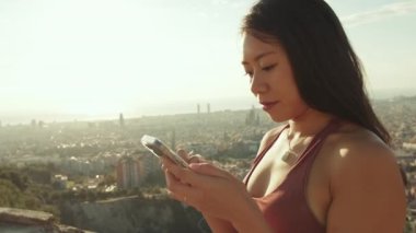 Kapalı, mutlu atletik kadın gözetleme noktasında dururken cep telefonu kullanıyor.