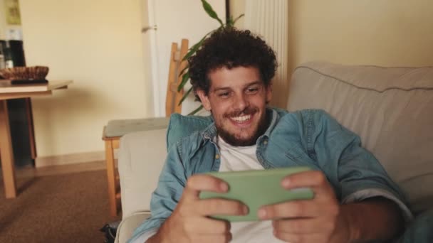 Uśmiechnięty Gracz Gra Gry Wideo Telefonem Komórkowym Leżącym Sofie — Wideo stockowe