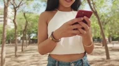 Şehir parkında yürürken cep telefonu kullanan tanınmayacak kadar güzel bir genç kadın.