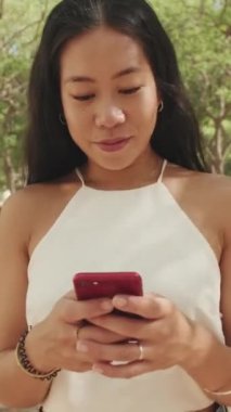 Şehir parkında yürürken cep telefonu kullanan güzel genç bayan.