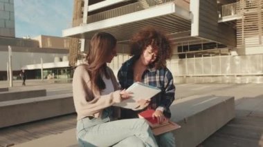 Girls share news and have fun sitting next to the university building