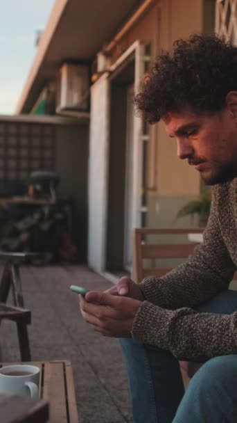 Χαμογελώντας Νεαρός Άνδρας Κάθεται Στη Βεράντα Χρησιμοποιεί Κινητό Τηλέφωνο — Αρχείο Βίντεο