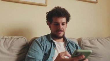Kanepede oturan gülümseyen adamın cep telefonuyla yakın plan fotoğrafı.
