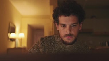 Yakın plan, genç adam bir dairede oturuyor, dizüstü bilgisayar kullanıyor.