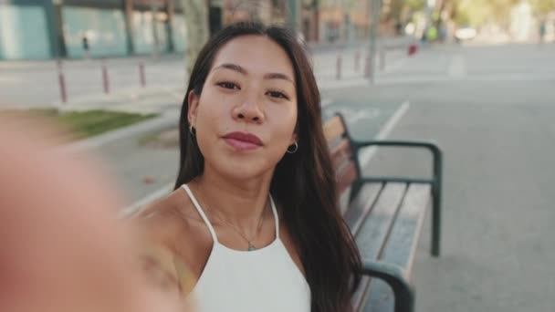 年轻女子坐在城市公园的长椅上 一边用手机自拍 — 图库视频影像