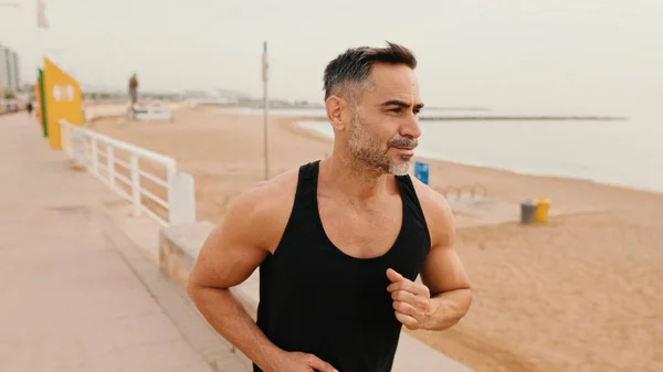 Middle-aged muscular man runs along the promenade before jogging