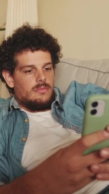 Kanepede yatarken mesaj yazan gülümseyen genç adam.