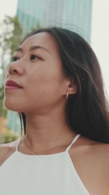 Kafasını çevirip modern şehrin arka planındaki kameraya bakan güzel genç bir kadının yakın çekimi.