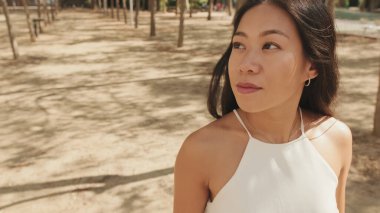 Beyaz bluzlu güzel esmer kız ve kot pantolon giyip hafta sonu şehir parkında yürümekten zevk alıyor.