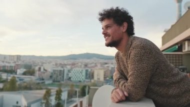 Gülümseyen genç adam balkonda duruyor.