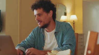 Genç adam evde otururken dizüstü bilgisayarda çalışıyor.