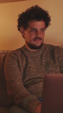 Genç adam oturma odasında kanepede dizüstü bilgisayarla oturuyor.