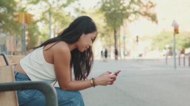 Genç kadın bankta oturuyor ve cep telefonu kullanıyor.