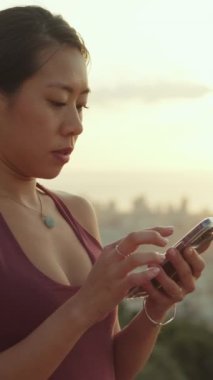 Şafak vakti gözetleme noktasında dururken cep telefonu kullanan mutlu atletik kadın.