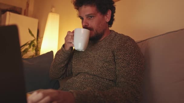 年轻人坐在客厅里的沙发上 拿着笔记本电脑 用杯子喝咖啡 — 图库视频影像