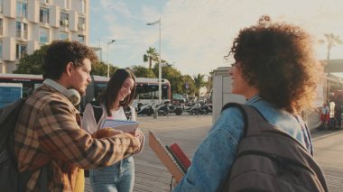 Bir grup öğrenci dışarıda dikilirken sohbet ediyorlar. Neşeli öğrenciler dışarıda kitap okuyup gülüyorlar.