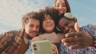 Mutlu gülen arkadaşlar cep telefonundan video görüşmesi yaparlar. Dört öğrenci selamlaşmak için el sallıyor.