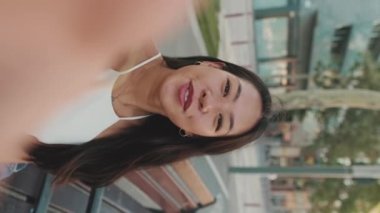 Şehir parkında bankta otururken cep telefonuyla video görüşmesi yapan genç bir kadın.