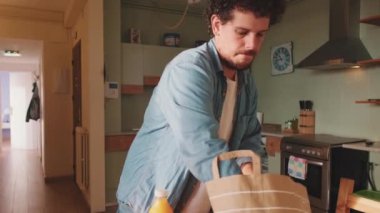 Genç adam mutfaktaki eşyalarını boşaltıyor.