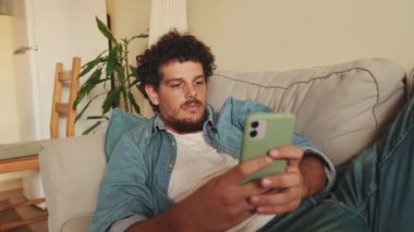 Genç adam kanepede yatarken mesaj yazıyor.