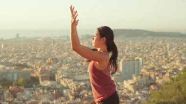 Kadın dışarıda yoga yapıyor, kollarını başının üstüne kaldırıyor.