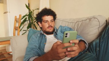 Mutlu adam akıllı telefonu elinde tutuyor, mesaj gönderiyor, sosyal ağlarda iletişim kuruyor, evde otururken internette geziniyor.