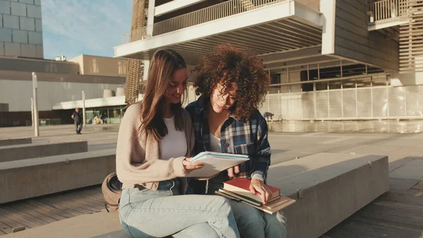 学生の女の子チャットや笑いの外に座っている 女の子はニュースを共有し 楽しい大学の建物の隣に座っている — ストック写真