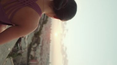 Yakından, vücut kıyafetli genç bir kadın güneş doğarken yoga yapıyor. Kız nilüfer pozisyonunda otururken ellerini kaldırır. Arka plan