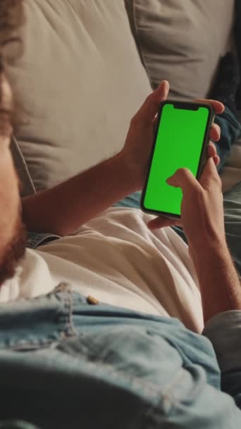 Молодой Человек Лежащий Диване Пользуется Мобильным Телефоном Зеленым Макетом Хромы — стоковое видео
