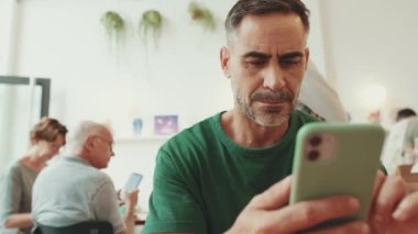 Kafede oturan orta yaşlı bir adam cep telefonu kullanıyor.