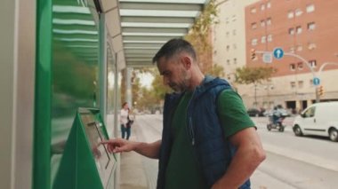 Orta yaşlı bir adam elektronik terminalde bilet ödüyor.