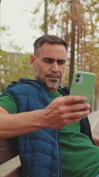 Μεσήλικας Τουρίστας Χρησιμοποιεί Κινητό Τηλέφωνο Ενώ Κάθεται Παγκάκι Πάρκο — Αρχείο Βίντεο