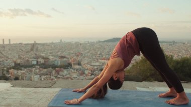 Genç bir kadın gün doğumunda izleme platformunda yoga yapıyor. Amanho mukha svanasana pozu