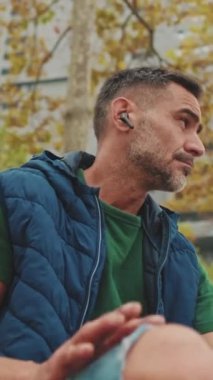 Orta yaşlı adam dinleniyor, parkta bankta otururken müzik dinliyor.