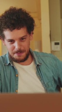 Genç bir erkek dizüstü bilgisayar kullanıyor, mutfakta serbest çalışıyor.