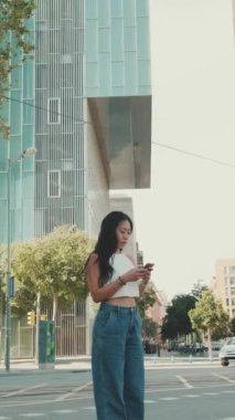 Genç kadın modern şehir arka planında dururken cep telefonunda harita uygulaması kullanıyor